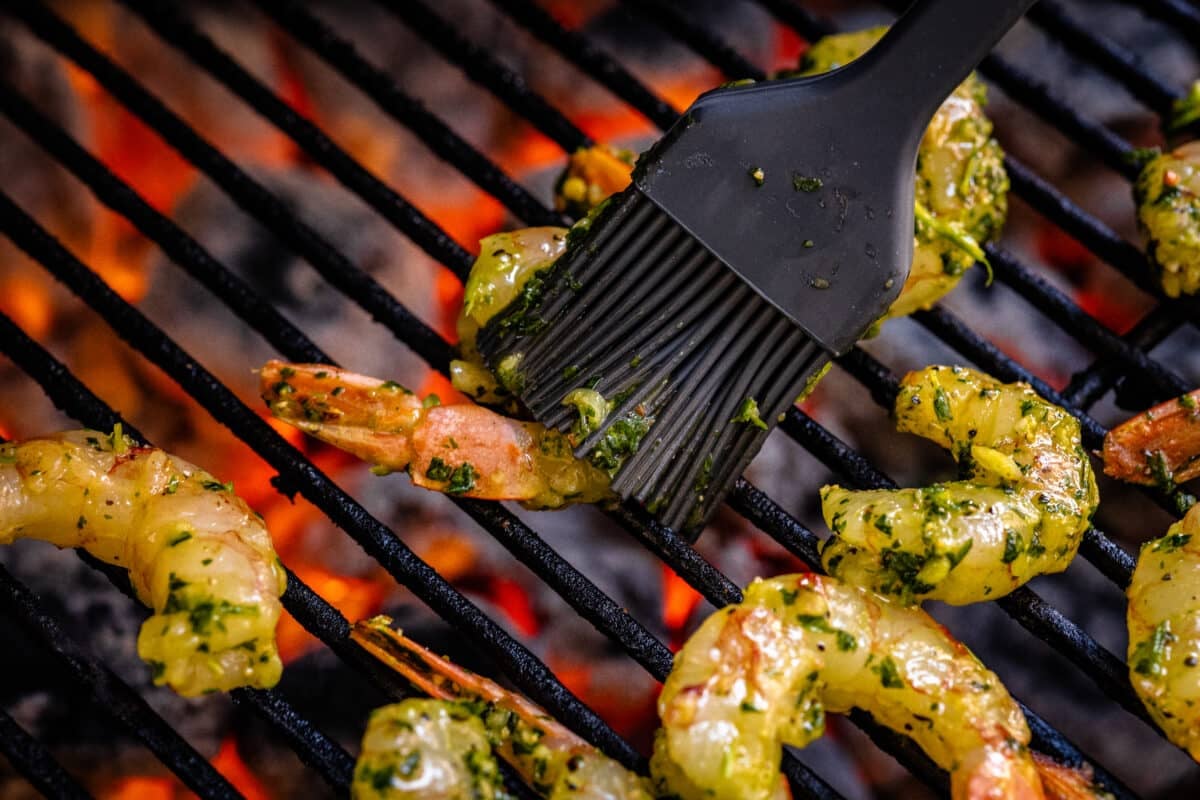Seafood on the grates of a grill being basted with a brush.
