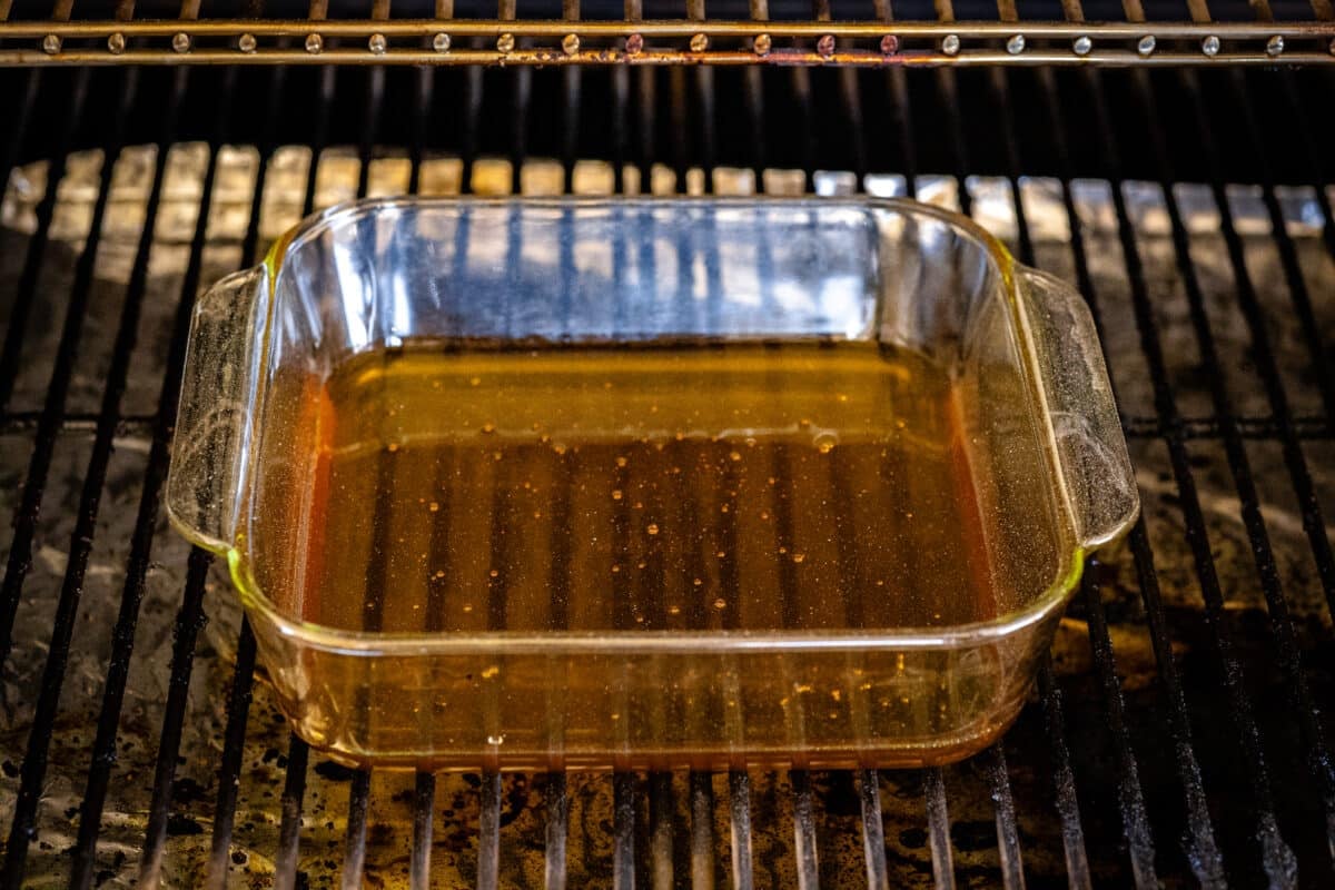 A transparent pan full of honey sitting on the grids of a grill.