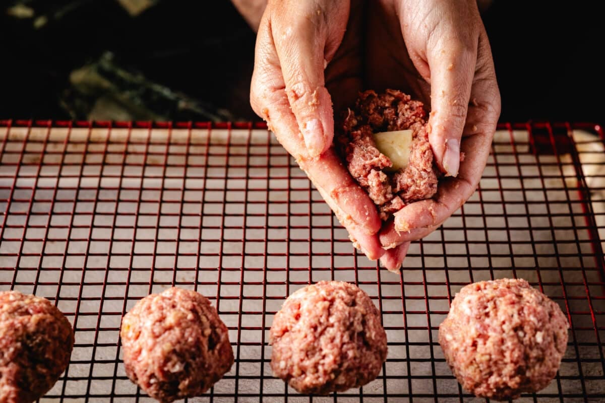 A chef's hands forming ground beef around a cube of cheese.