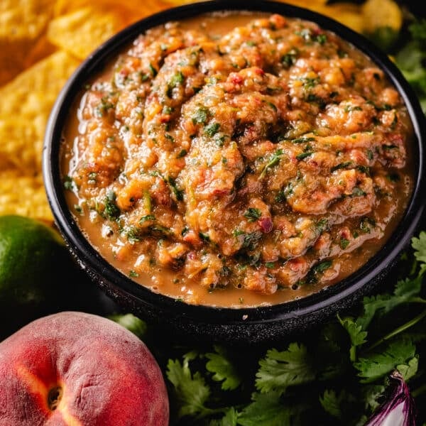 A black bowl full of salsa next to chips and raw ingredients.