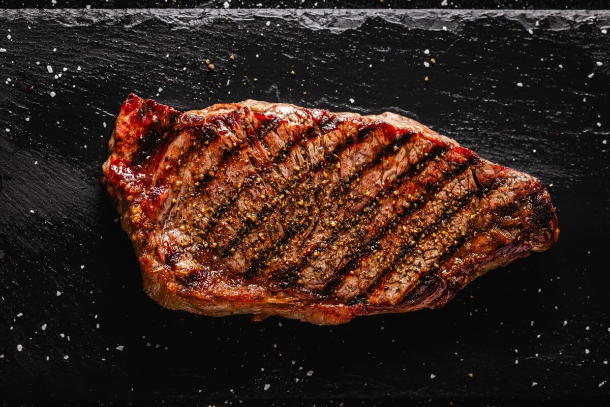 A grilled New York strip steak on a black stone platter.