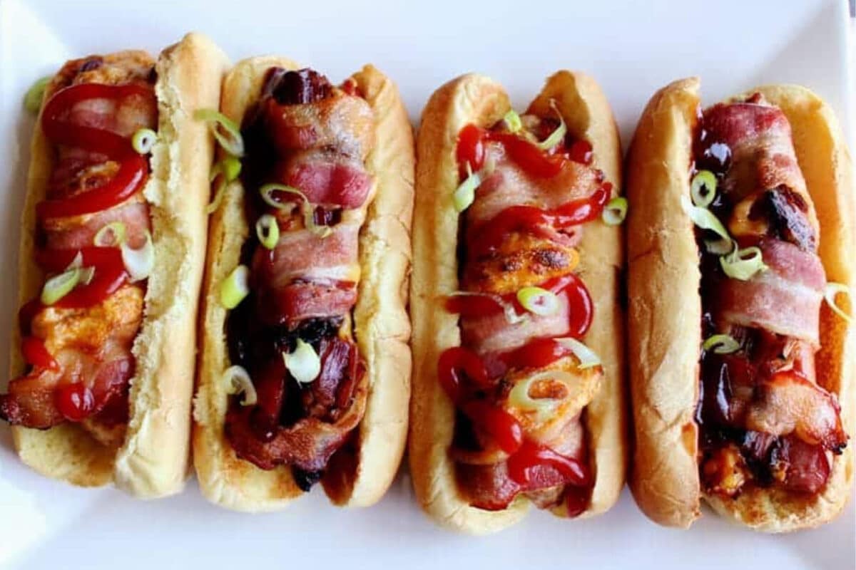 A white plate lines with four stuffed hot dogs.