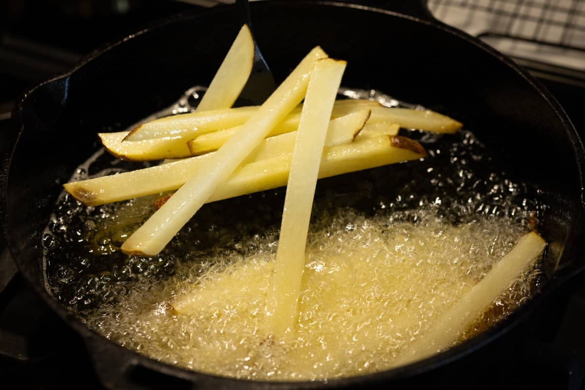 Julienned potatoes cooling in oil in a cast iron pan.