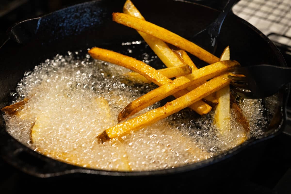 Fries cooking in oil in a cast iron pan.