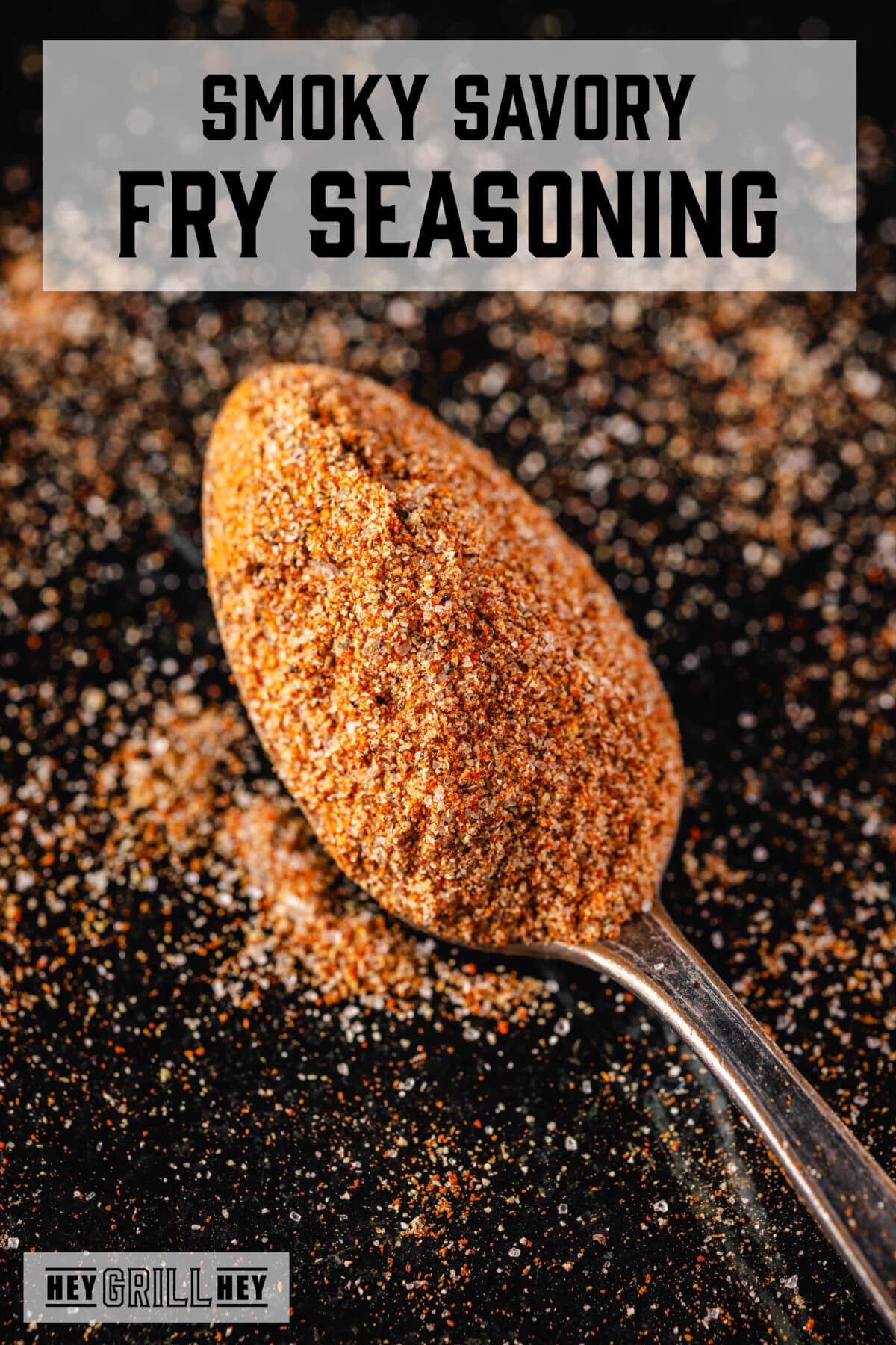 A closeup shot of a spoon with a scoop of seasoning. The text overlay reads "Smoky Savory Fry Seasoning" at the top, and "Hey Grill Hey" at the bottom.