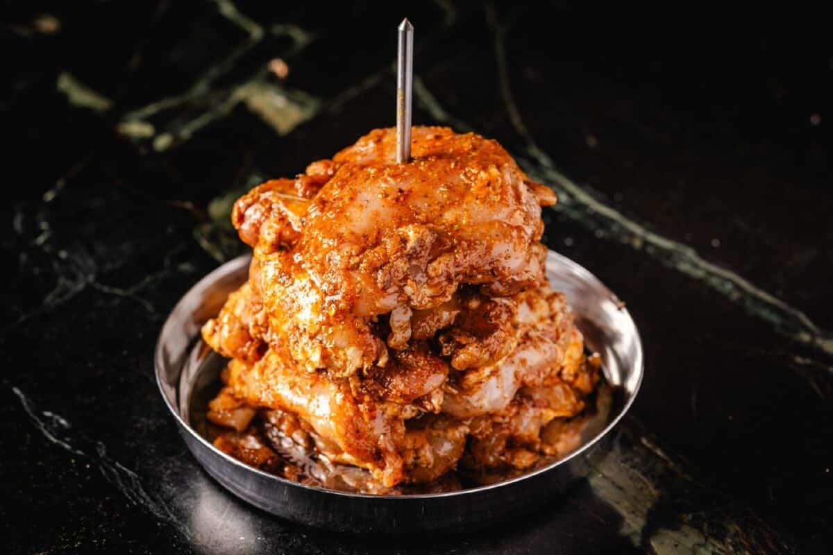 Seasoned chicken thighs stacked on a trompo.