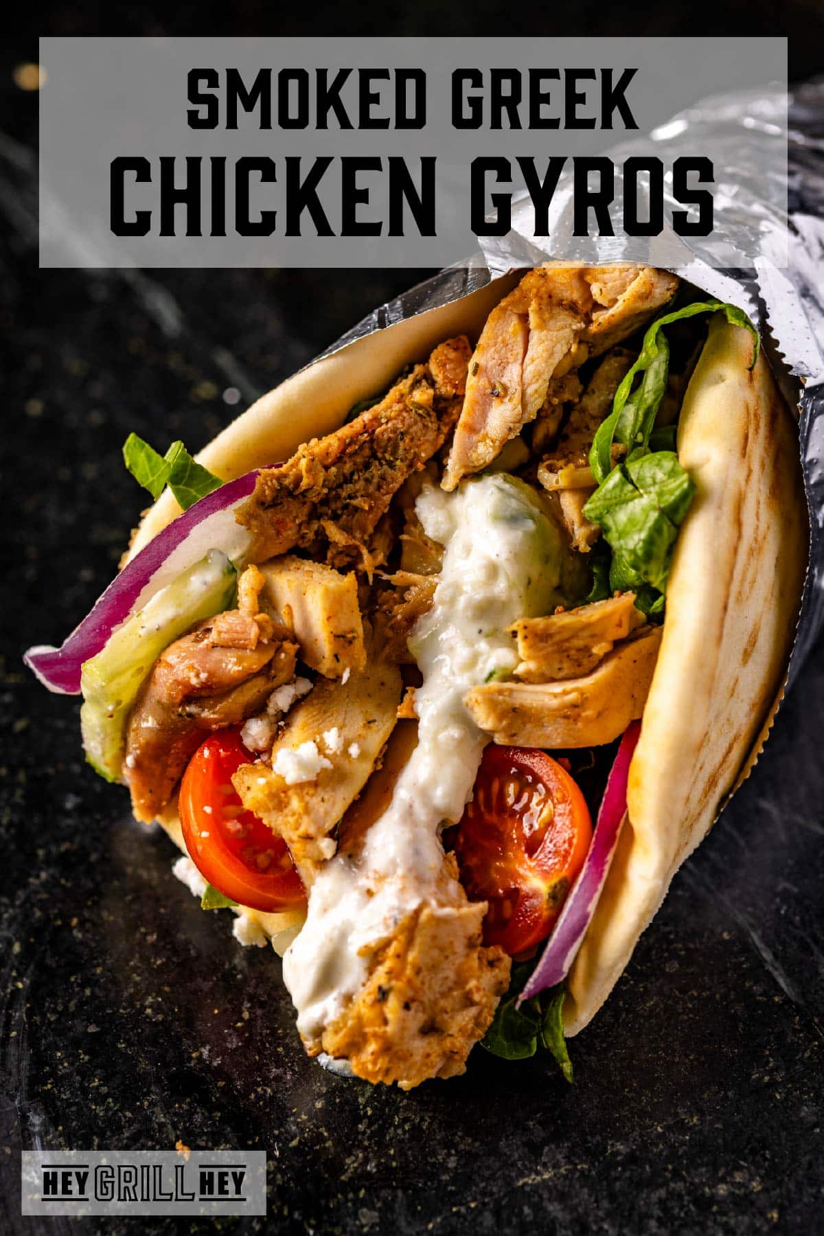 A chicken gyro partially wrapped in foil on a dark surface. The text overlay reads "Smoked Greek Chicken Gyros" at the top, and "Hey Grill Hey" at the bottom.
