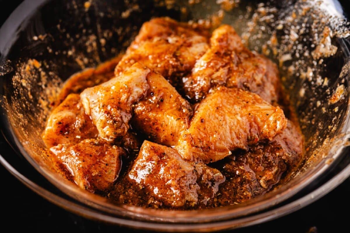 A clear glass bowl filled with marinated chicken cubes.