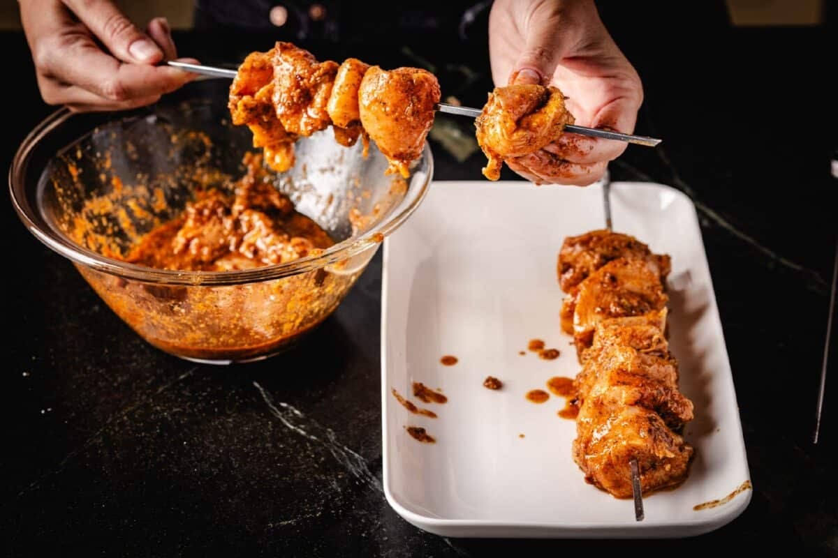 A chef's hands skewering cubed chicken above a white plate.