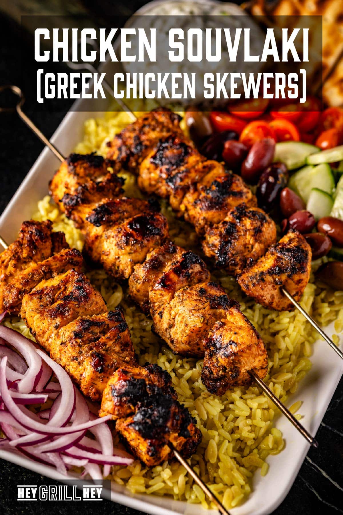 A platter of skewered chicken on a bed of rice with fresh tomato and cucumber as a garnish. The text overlay reads "Chicken Souvlaki (Greek Chicken Skewers)" at the top, and "Hey Grill Hey" at the bottom.