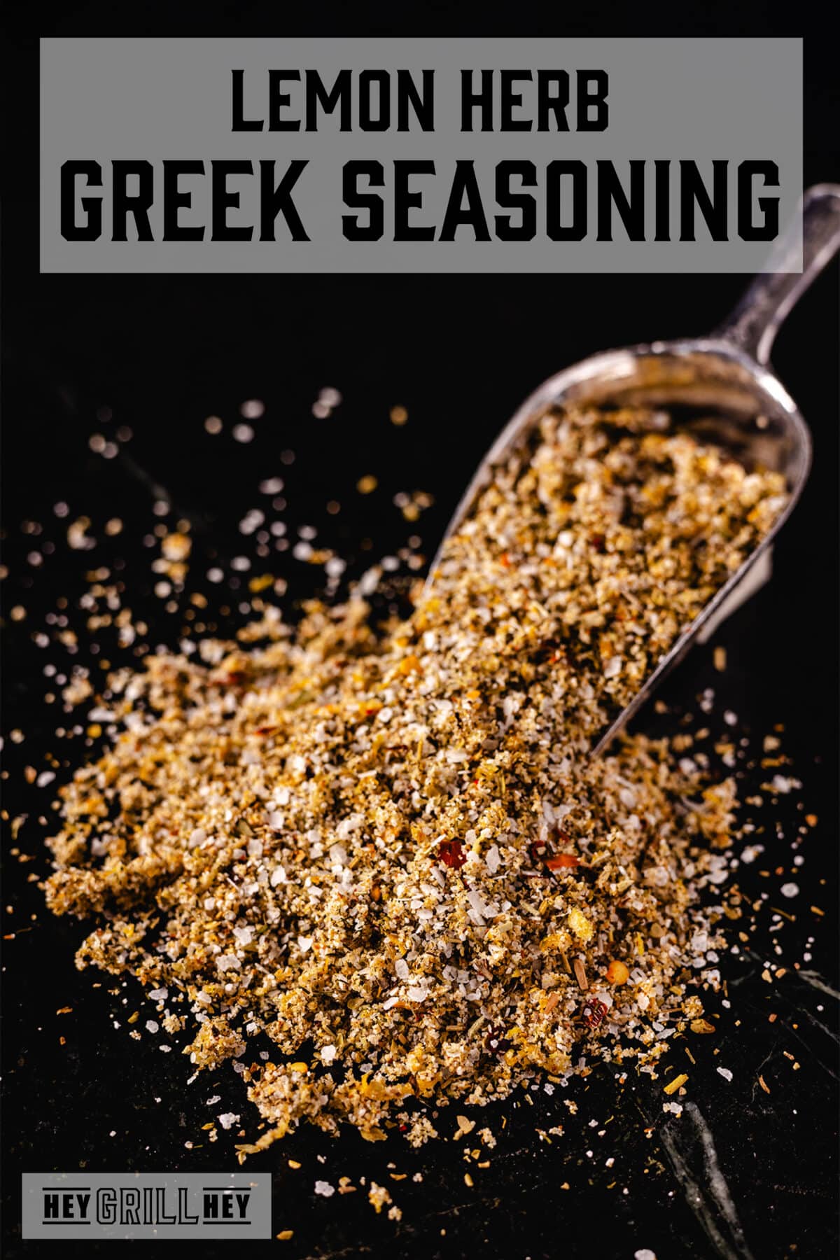 A pile of Greek seasoning spilling out from a metal scoop onto a black surface. The text overlay reads "Lemon Herb Greek Seasoning" at the top, and "Hey Grill Hey" at the bottom.