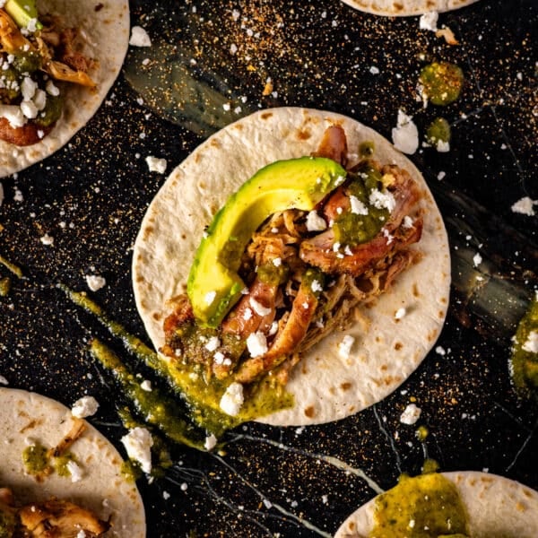 A closeup shout of a smoked and shredded chicken taco topped with an avocado slice and green salsa.