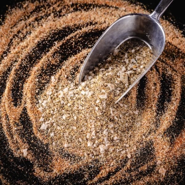 A metal scoop in all-purpose seasoning piled on a dark surface.