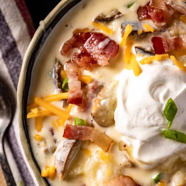 A closeup shot of a bowl of soup topped with shredded cheese, bacon bits, and a dollop of sour cream.