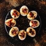 A round, black plate with bacon deviled eggs in a circle.
