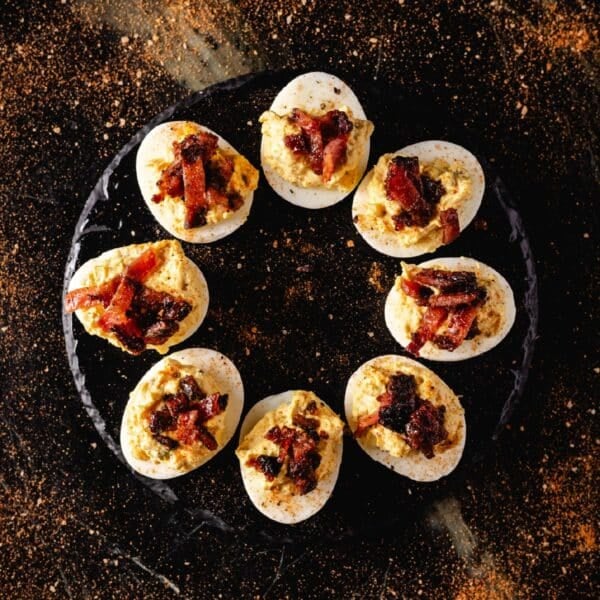 A round, black plate with bacon deviled eggs in a circle.