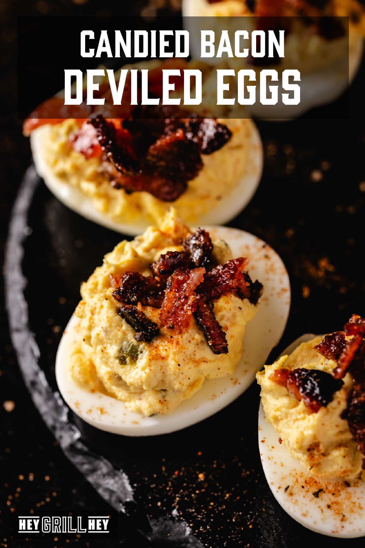 A closeup shot of four bacon deviled eggs on a black plate. The text overlay reads "Smoked Bacon Deviled Eggs" at the top, and "Hey Grill Hey" at the bottom.