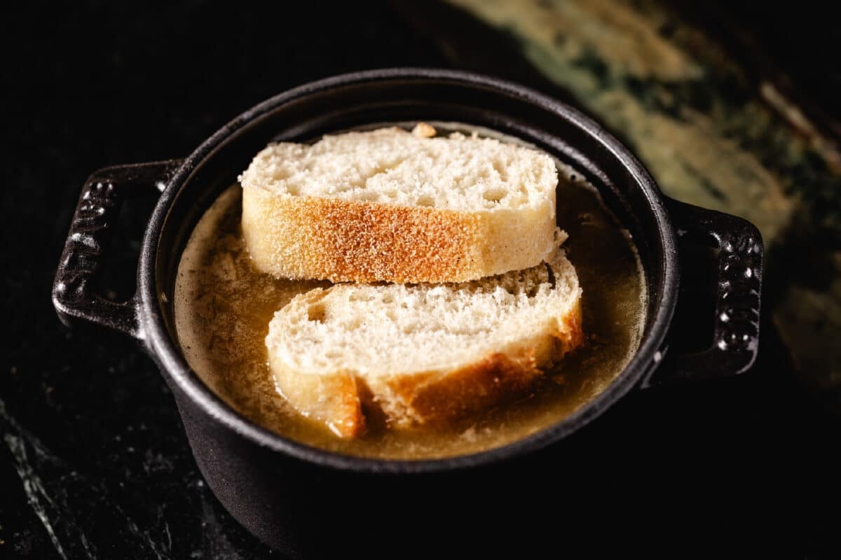 Two slices of baguette bread sitting on broth in a small cast iron pot.