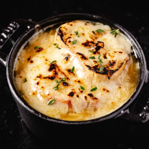 A closeup shot of a cast iron bowl filled with French onion soup.
