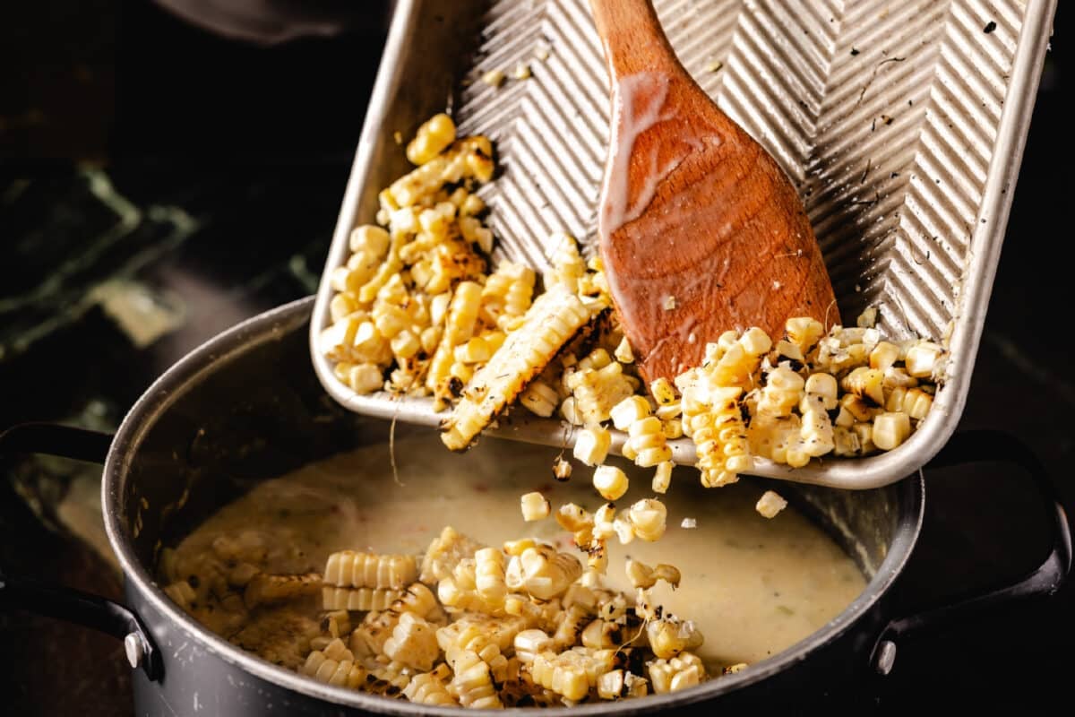 Sliced kernels on a baking sheet being moved to a large pot below using a wooden spatula.