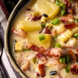 A bowl of corn, potato, and bacon soup, and a spoon resting on a striped, cloth napkin.