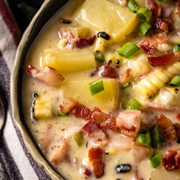 A bowl of corn, potato, and bacon soup, and a spoon resting on a striped, cloth napkin.