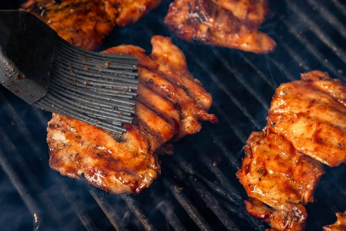 A rubber brush basting poultry thighs sitting on the grates of a smoker.