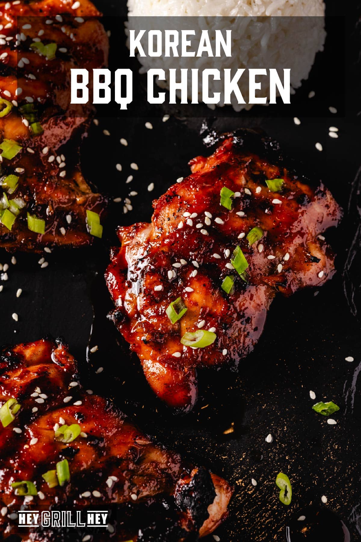 Smoked chicken thighs topped with sliced green onions and sesame seeds, and a scoop of rice on a black platter. The text overlay reads "Korean BBQ Chicken" at the top, and "Hey Grill Hey" at the bottom.