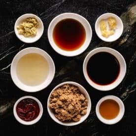 Eight bowls of liquid and granulated ingredients for a Korean BBQ marinade sitting on a marble countertop.