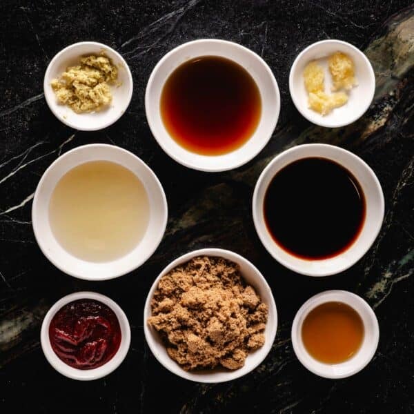 Eight bowls of liquid and granulated ingredients for a Korean BBQ marinade sitting on a marble countertop.