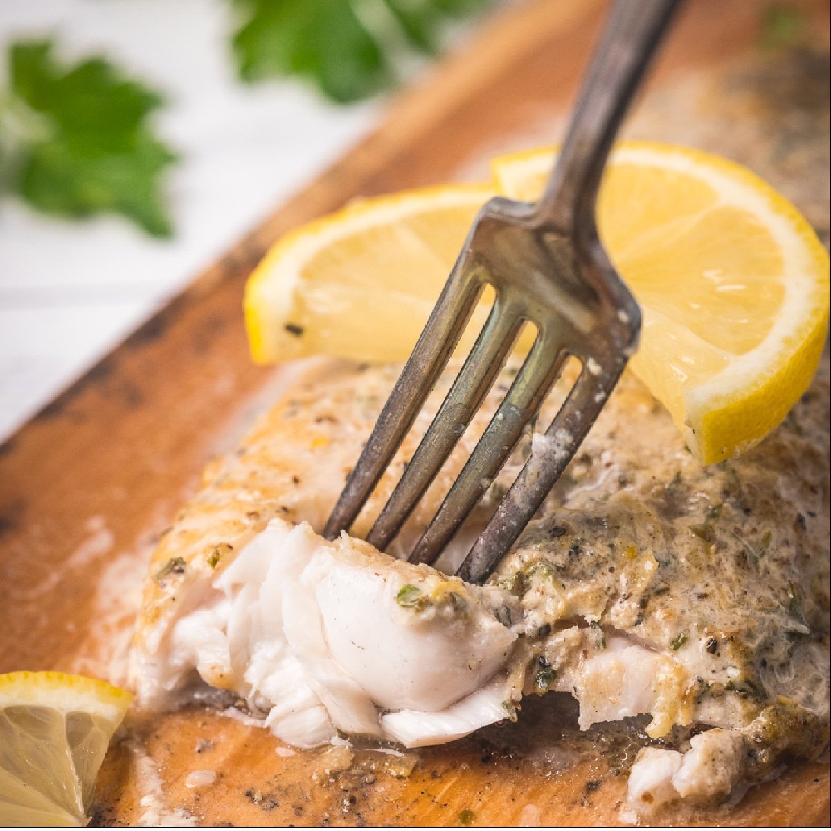 A fork flaking a piece out of a grilled catfish filet on a wooden serving platter.