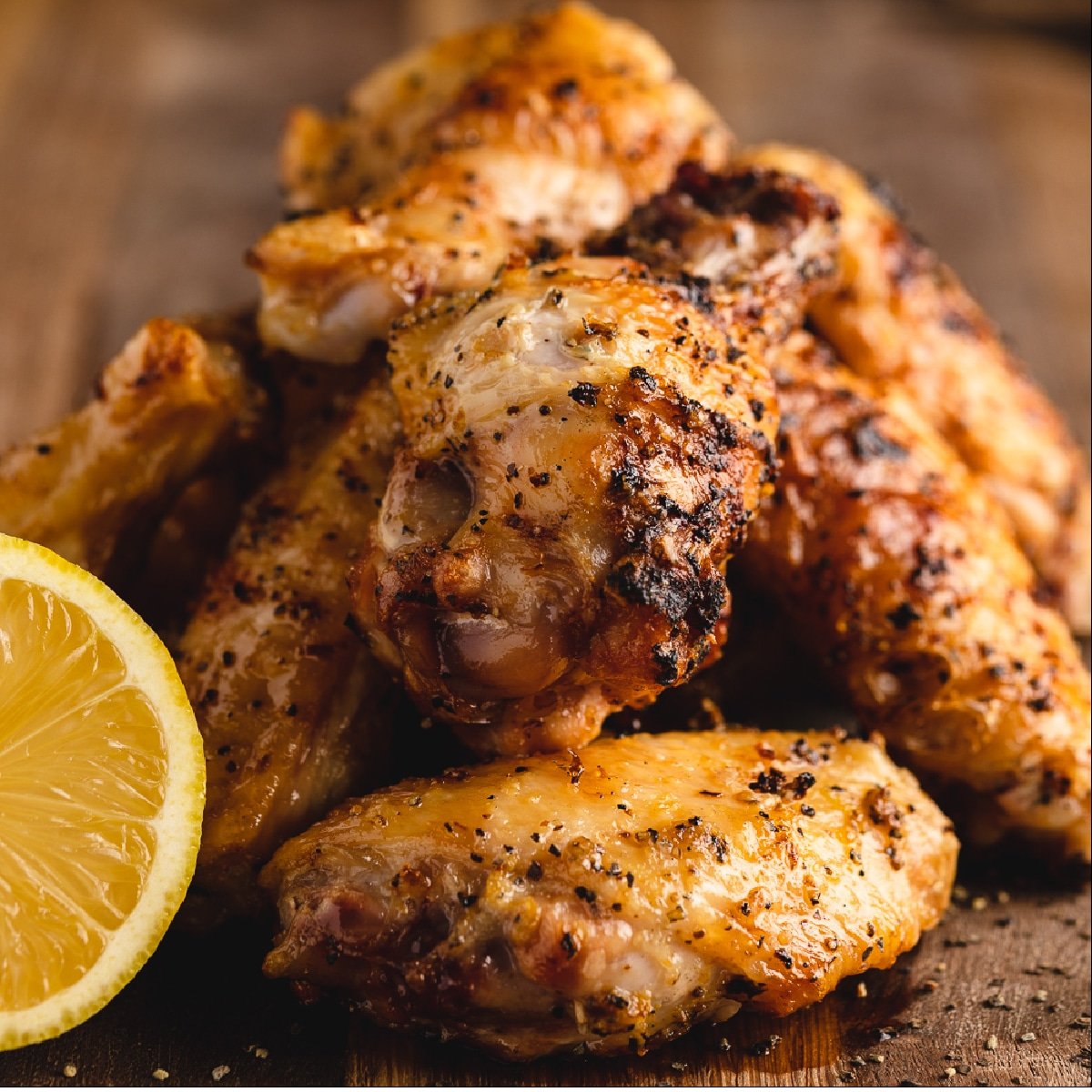 Grilled chicken wings stacked on a wooden cutting board with a slice of lemon.