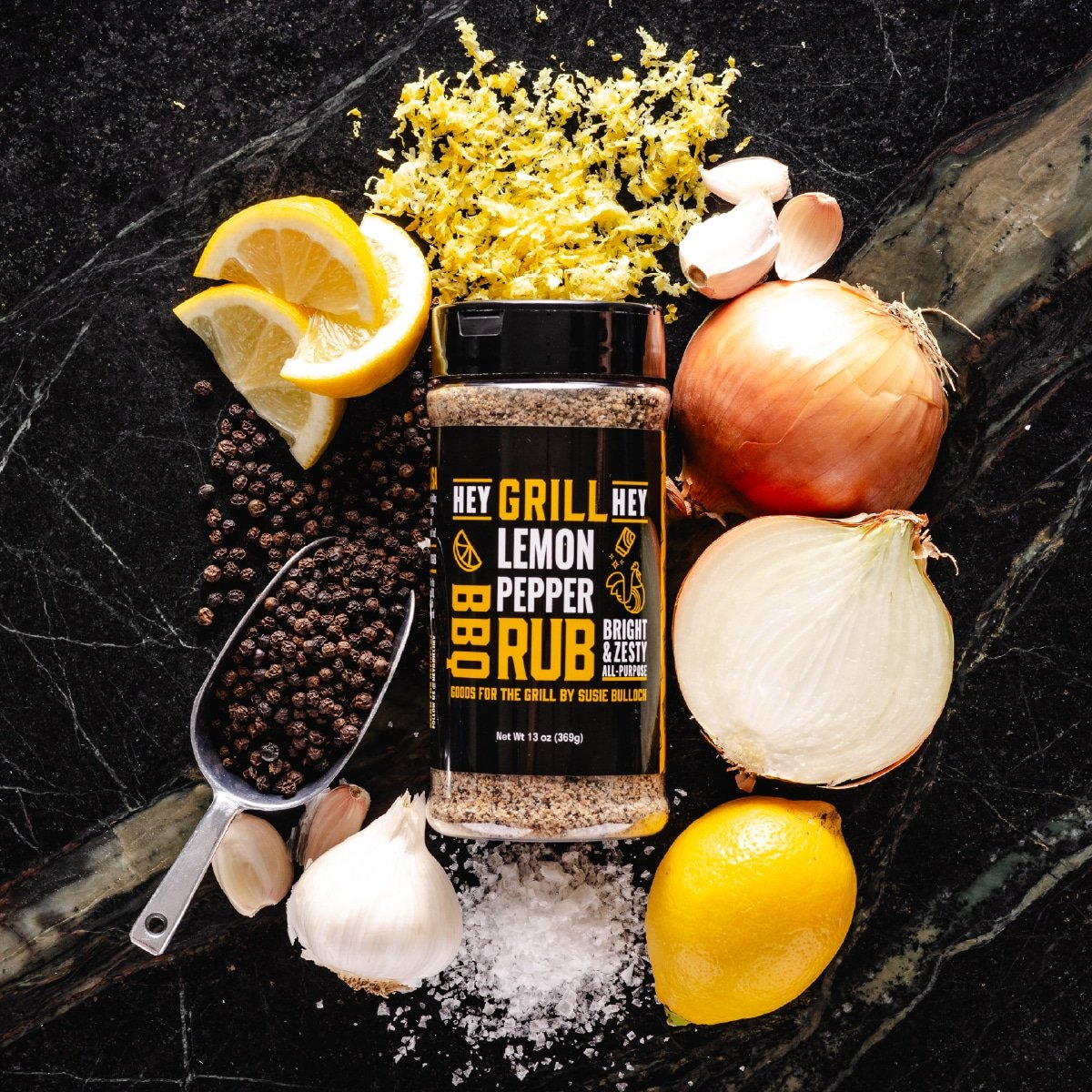 A bottle of Hey Grill Hey Lemon Pepper Rub on a marble surface surrounded by the recipe ingredients.