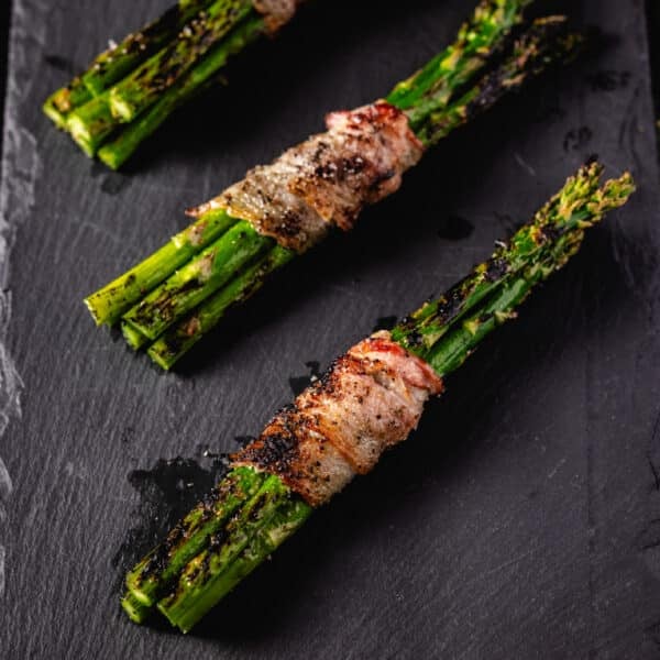 Three bacon-wrapped bundles of asparagus resting on a black plate.