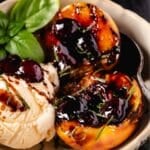A bowl with peach halves and a scoop of vanilla ice cream topped with a cherry glaze, and a mint garnish.