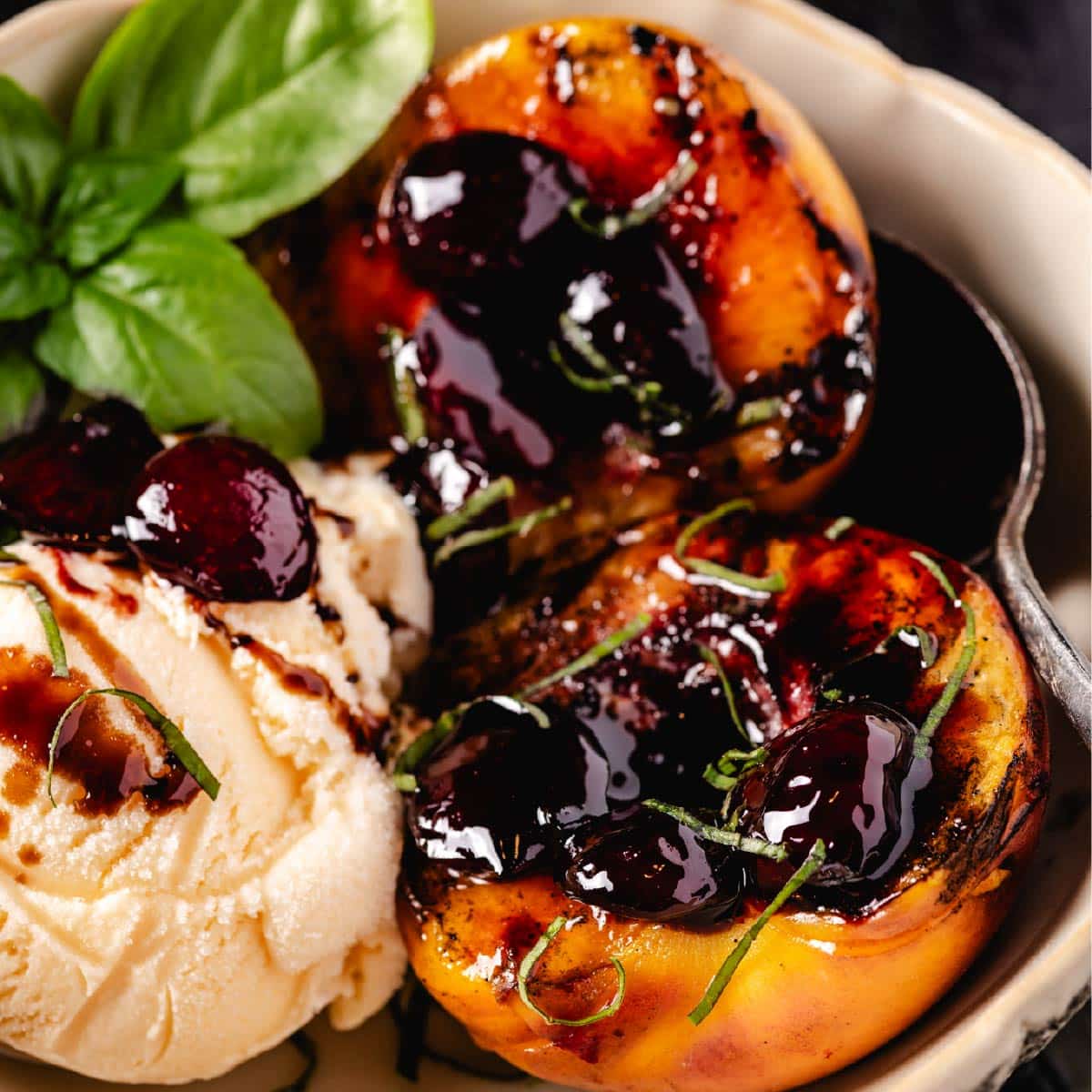 A bowl with peach halves and a scoop of vanilla ice cream topped with a cherry glaze, and a mint garnish.
