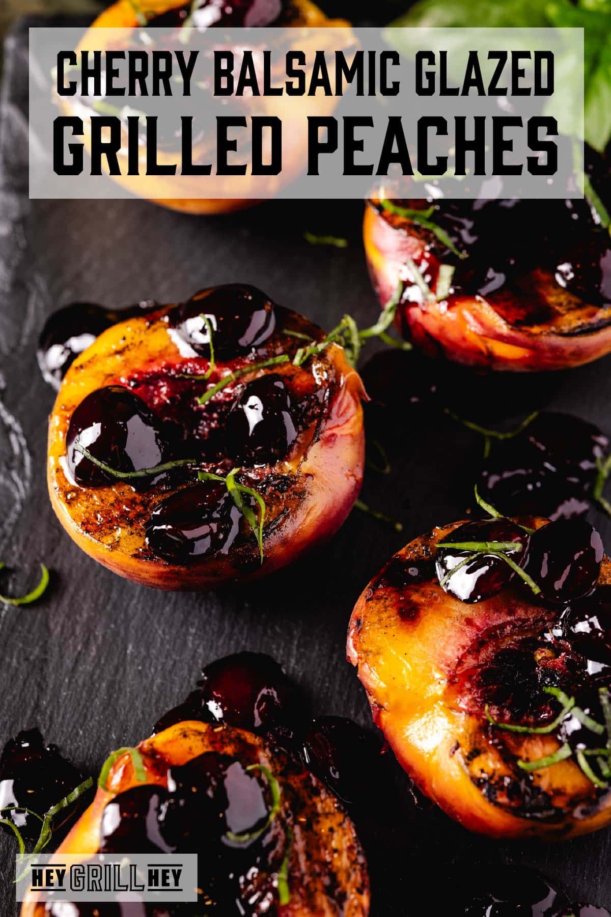 Grilled Peaches with a Cherry Balsamic Glaze Five peach halves topped with a cherry glaze on a black platter. The text overlay reads "Cherry Balsamic Glazed Grilled Peaches" at the top, and "Hey Grill Hey" at the bottom.