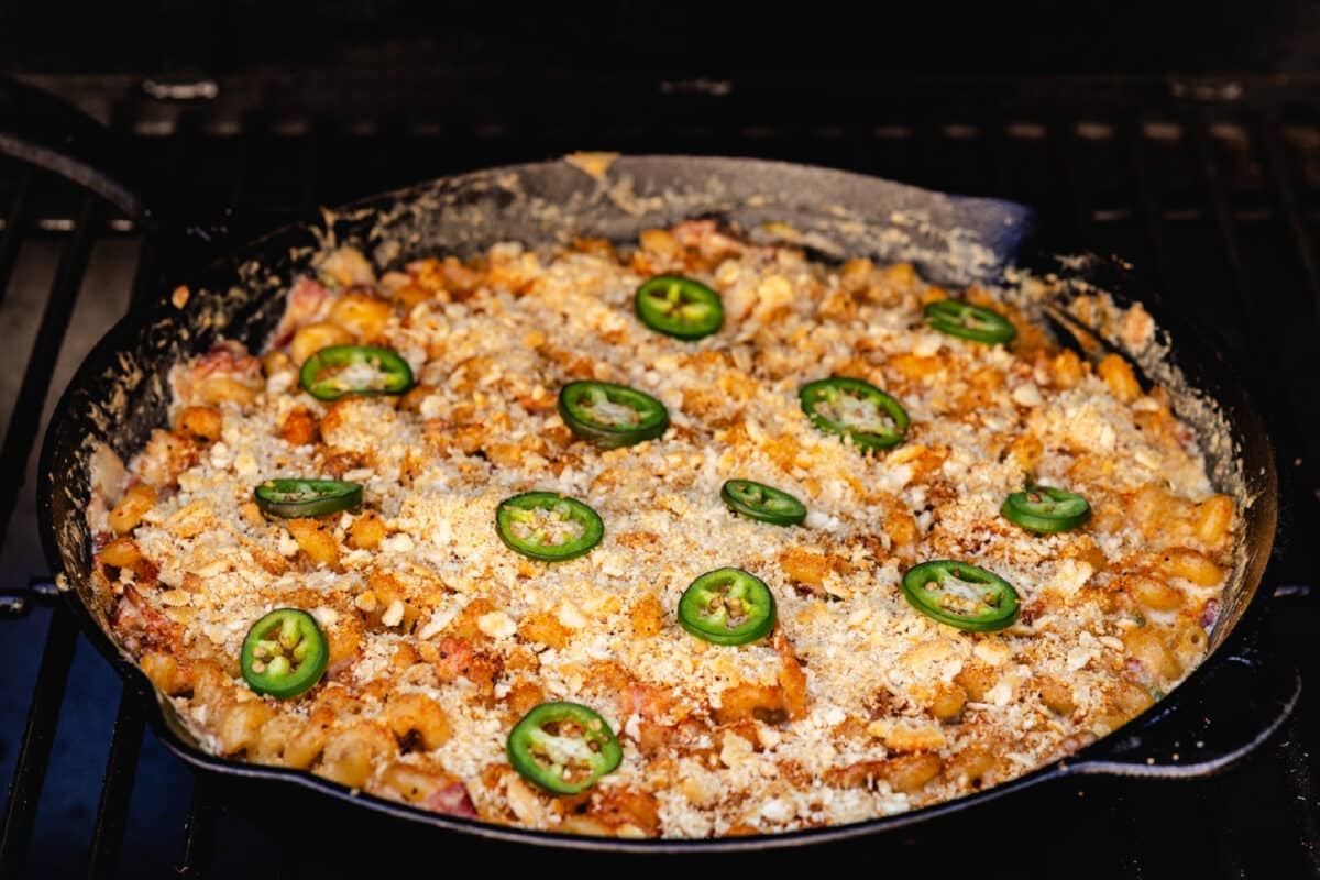 A cast iron skillet filled with a pasta and jalapeño dish on the grates of a smoker.