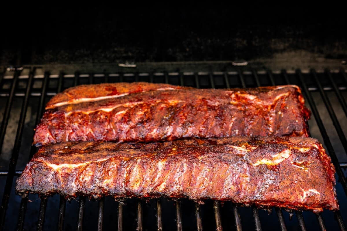 Two racks of baby backs sitting on the grates of a smoker.
