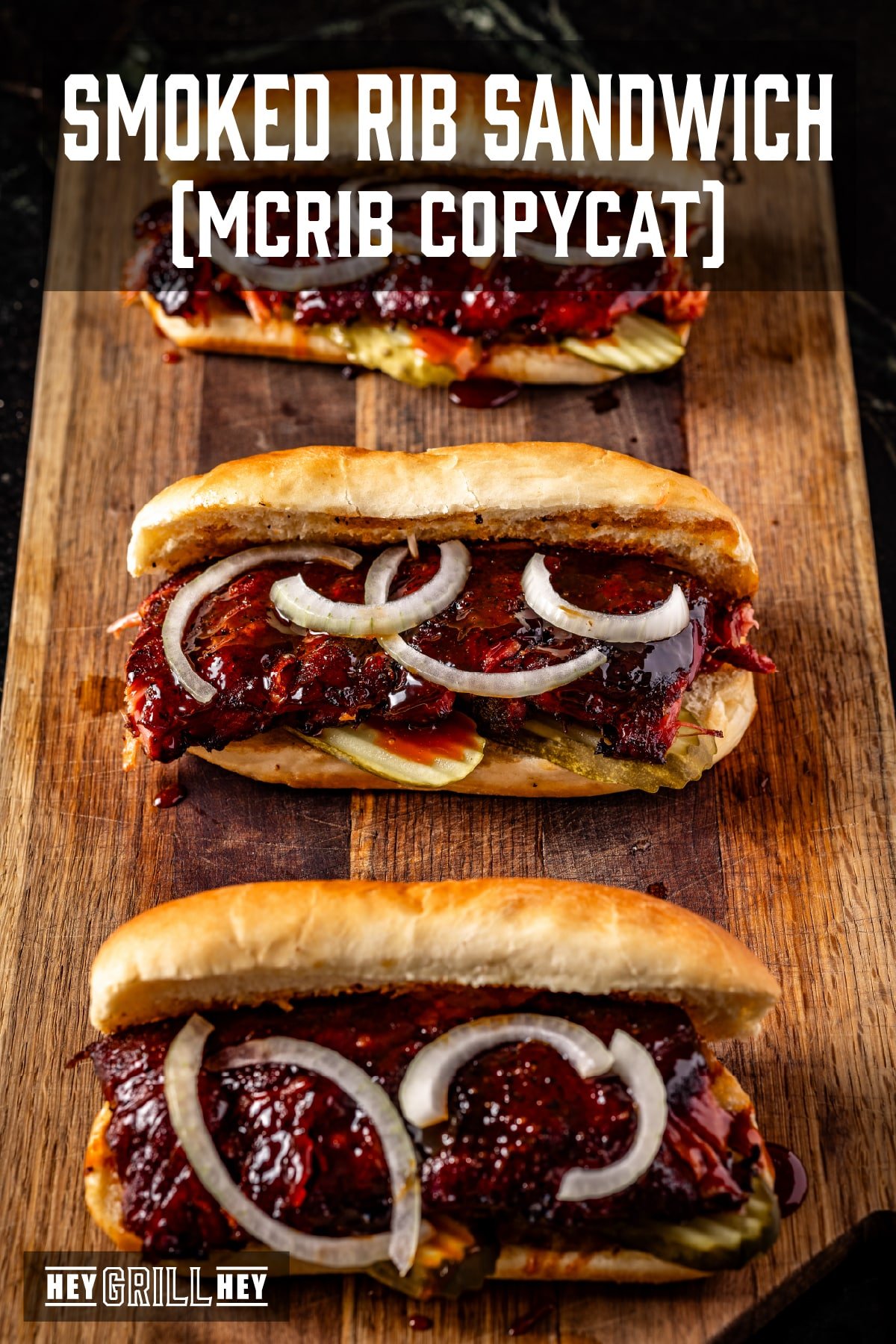 Three rib sandwiches with sliced onions and pickles resting on a wooden cutting board. The text overlay reads "Smoked Rib Sandwich (McRib Copycat)" at the top, and "Hey Grill Hey" at the bottom.