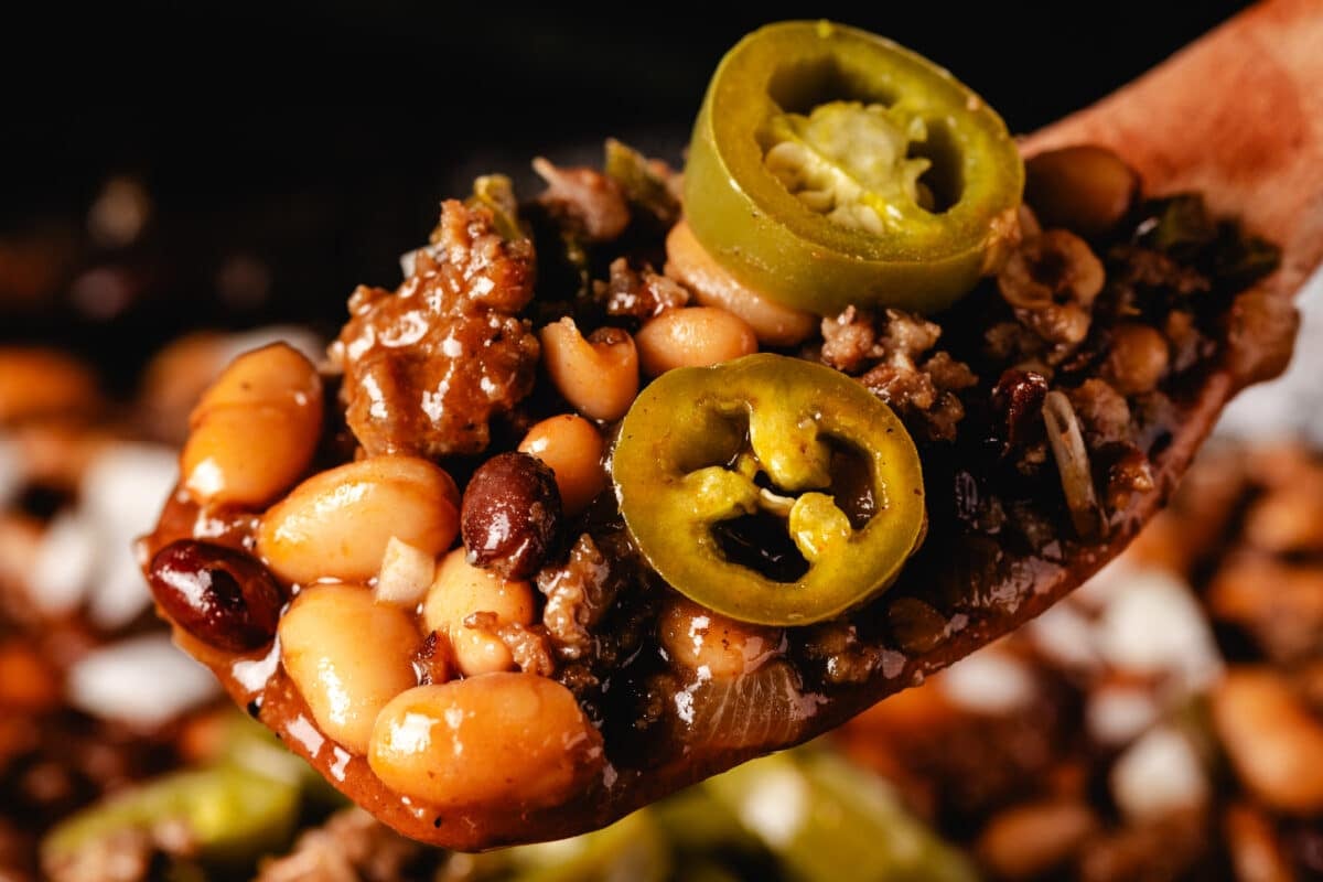 A scoop of a pit beans recipe seasoned with Sweet Rub on a wooden spatula.