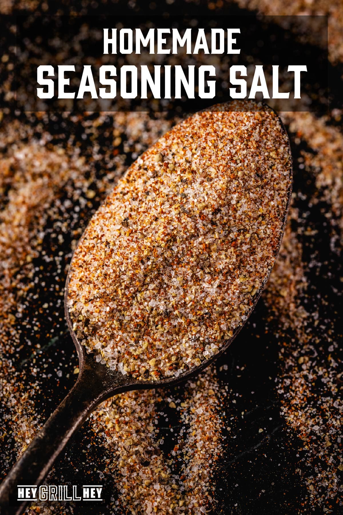 A spoon with a heaping scoop of seasoning on a counter dusted with the seasoning. The text overlay reads "Homemade Seasoning Salt" at the top, and "Hey Grill Hey" at the bottom.