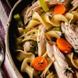 A close up shot of a bowl filled with chicken noodle soup.