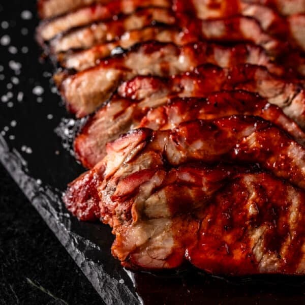 Slices of pork char siu shingled on a black patter and drizzled with BBQ sauce.