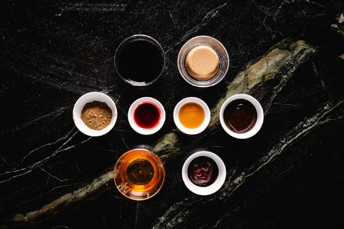 An overhead shot of 8 glass bowls in rows of 2, 4, and 2 filled with individual ingredients for a sauce.