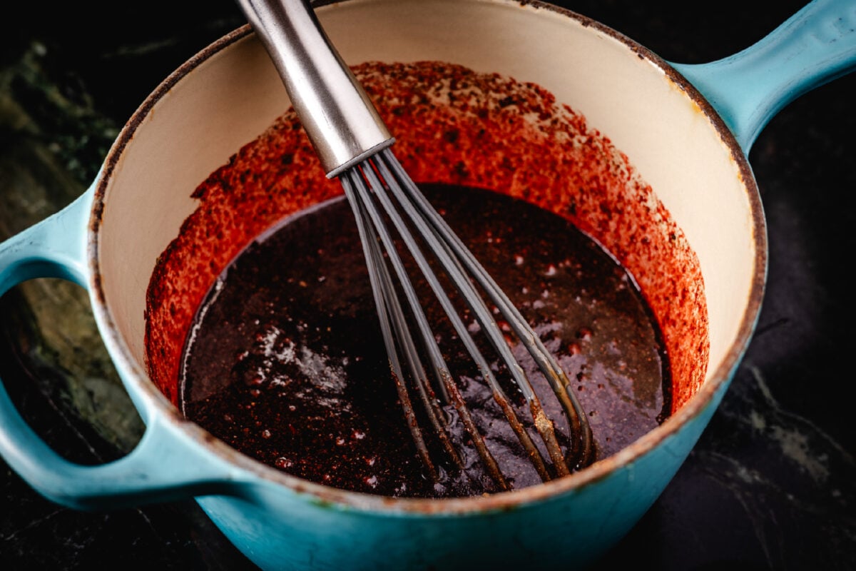 A whisk resting in a blue pot of sauce.